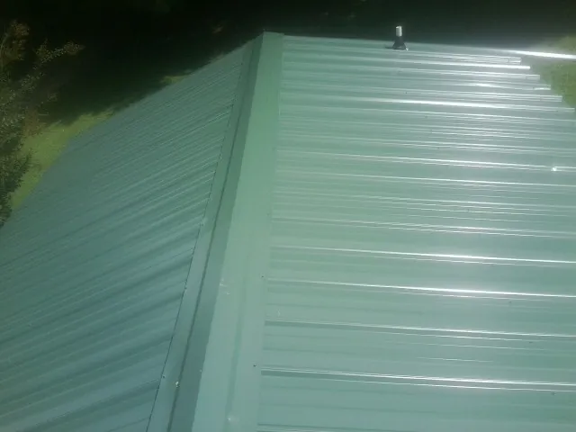 New green metal panels meeting at the ridge of a roof — Flat Roof Repair work by our crew in Willingboro
