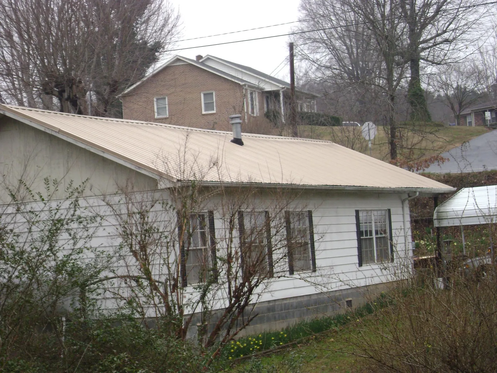 Tan metal roof on a white sided house set into a hillside — Commercial Roofing by Roofing Brothers in Willingboro
